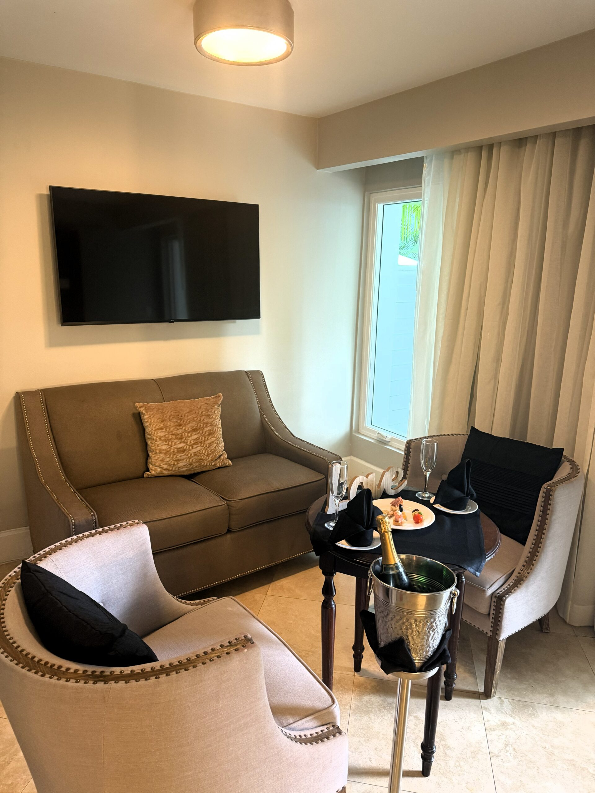 Separate sitting area at the Sandals Royal Bahamian Island Village One Bedroom Walkout Butler Villa Suite with HD Smart TV, love seat, chairs, and butler-arranged champagne
