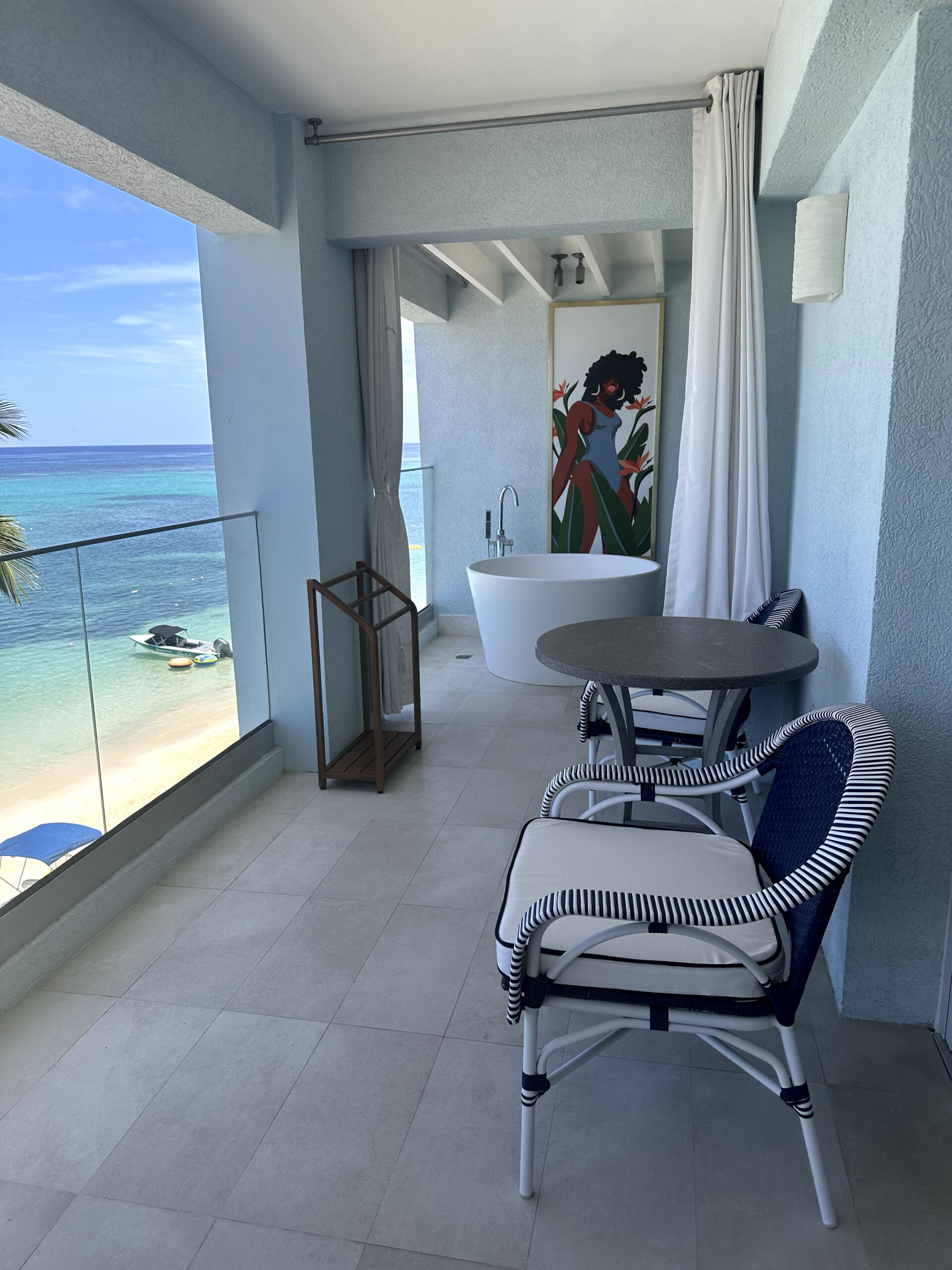 Private balcony with a Tranquility soaking tub for two, bistro table, and ocean view at the Mammee Bay Beachfront One Bedroom Butler Suite (B1B) at Sandals Dunn's River