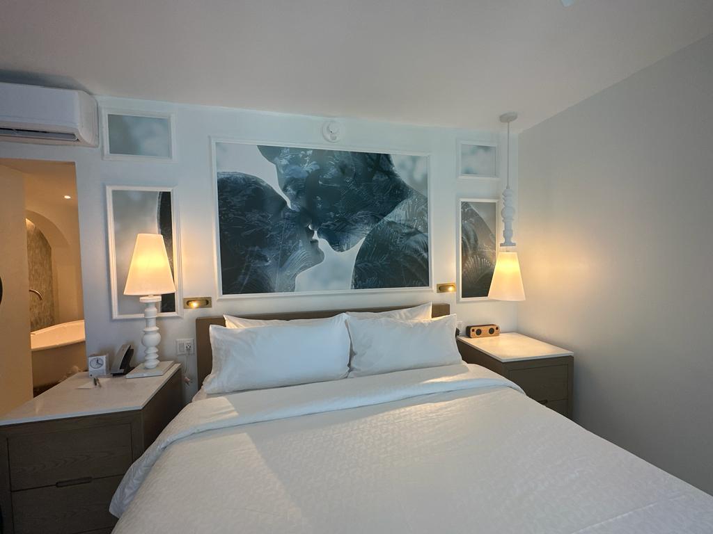 King bed with tropical wall art in the Mammee Bay Beachfront One Bedroom Butler Suite (B1B) at Sandals Dunn's River.