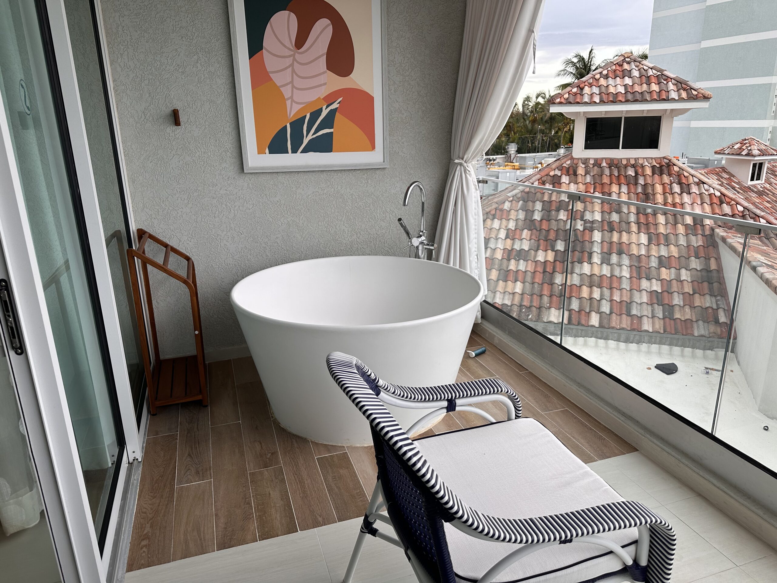 Balcony Tranquility Soaking Tub on the private balcony of the Travertine Beachfront Club Level Room at Sandals Dunn's River, with a lounge chair and rooftop view.