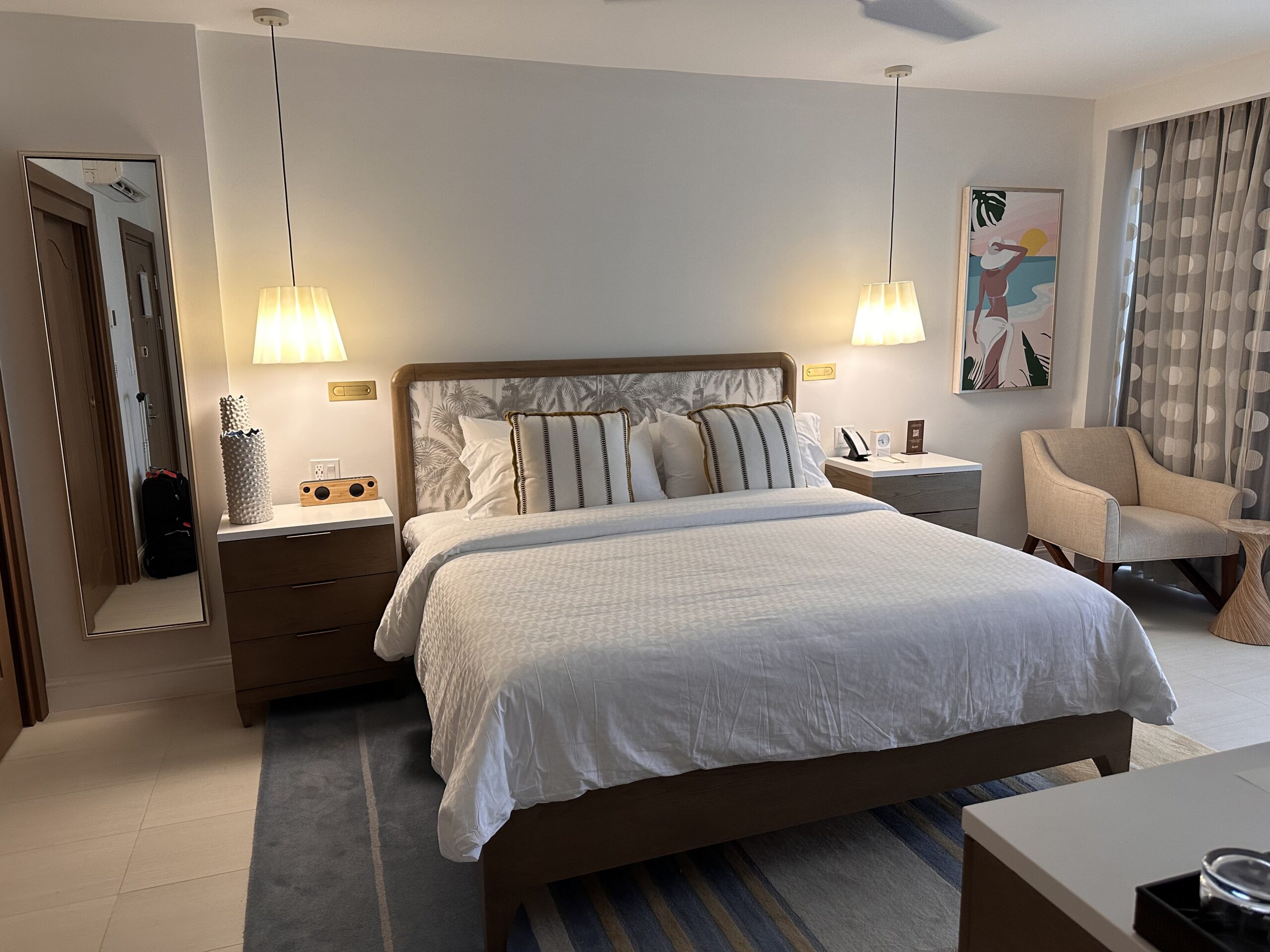 Bedroom in the Travertine Beachfront Club Level Room at Sandals Dunn's River with a king bed, upholstered palm-print headboard, and tropical artwork on the wall.