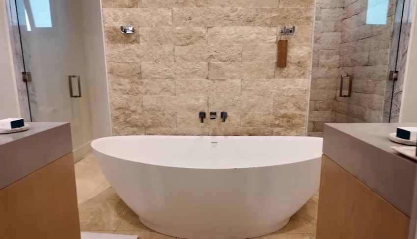 Bathroom in the Beachfront One-Bedroom Butler Villa Suite with Private Pool (BVJP) at Sandals Saint Vincent, with a freestanding soaking tub, stone feature wall, and dual vanities