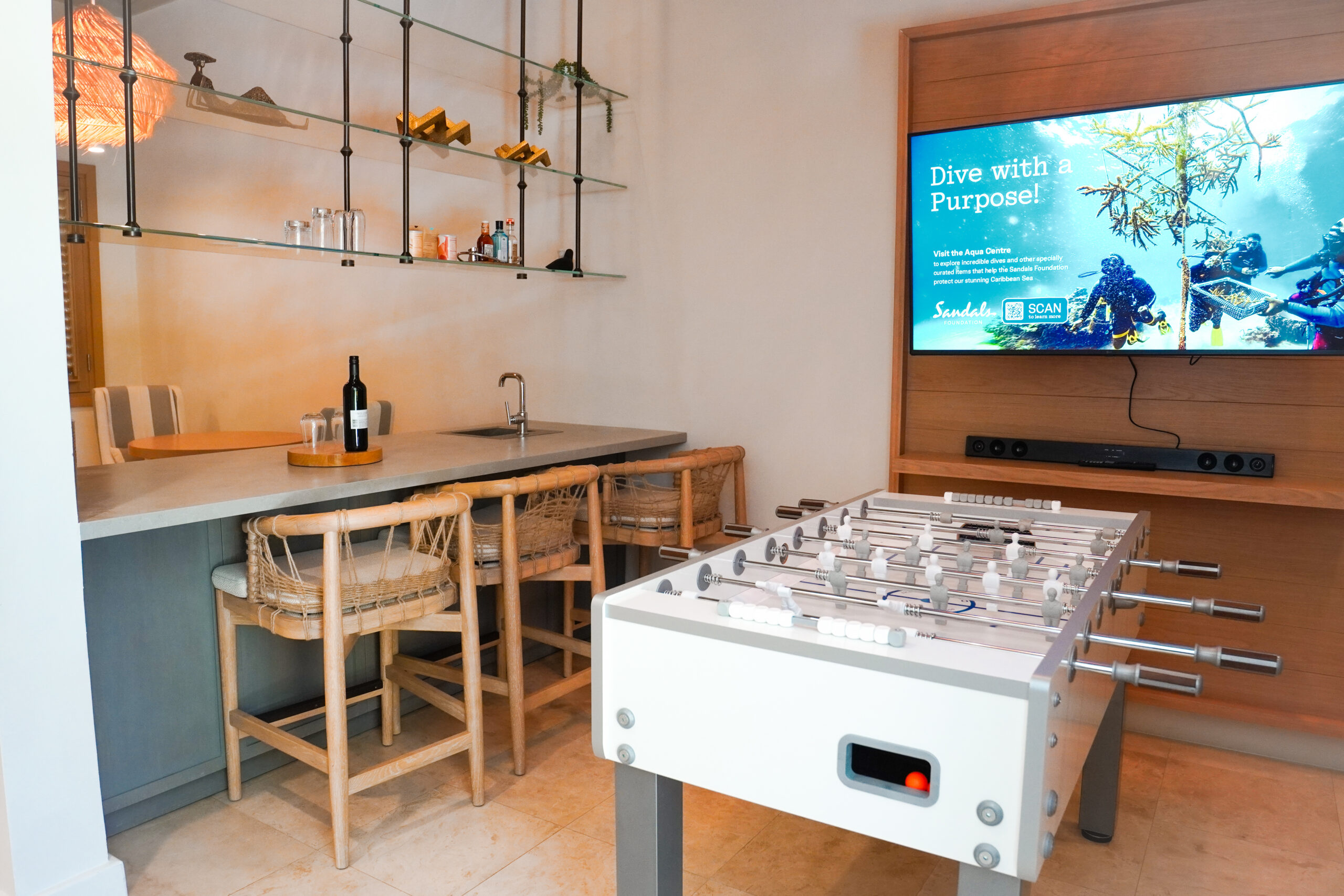 Games and entertainment area in the Beachfront One-Bedroom Butler Villa Suite with Private Pool (BVJP) at Sandals Saint Vincent, with a foosball table, wet bar, and wall-mounted TV