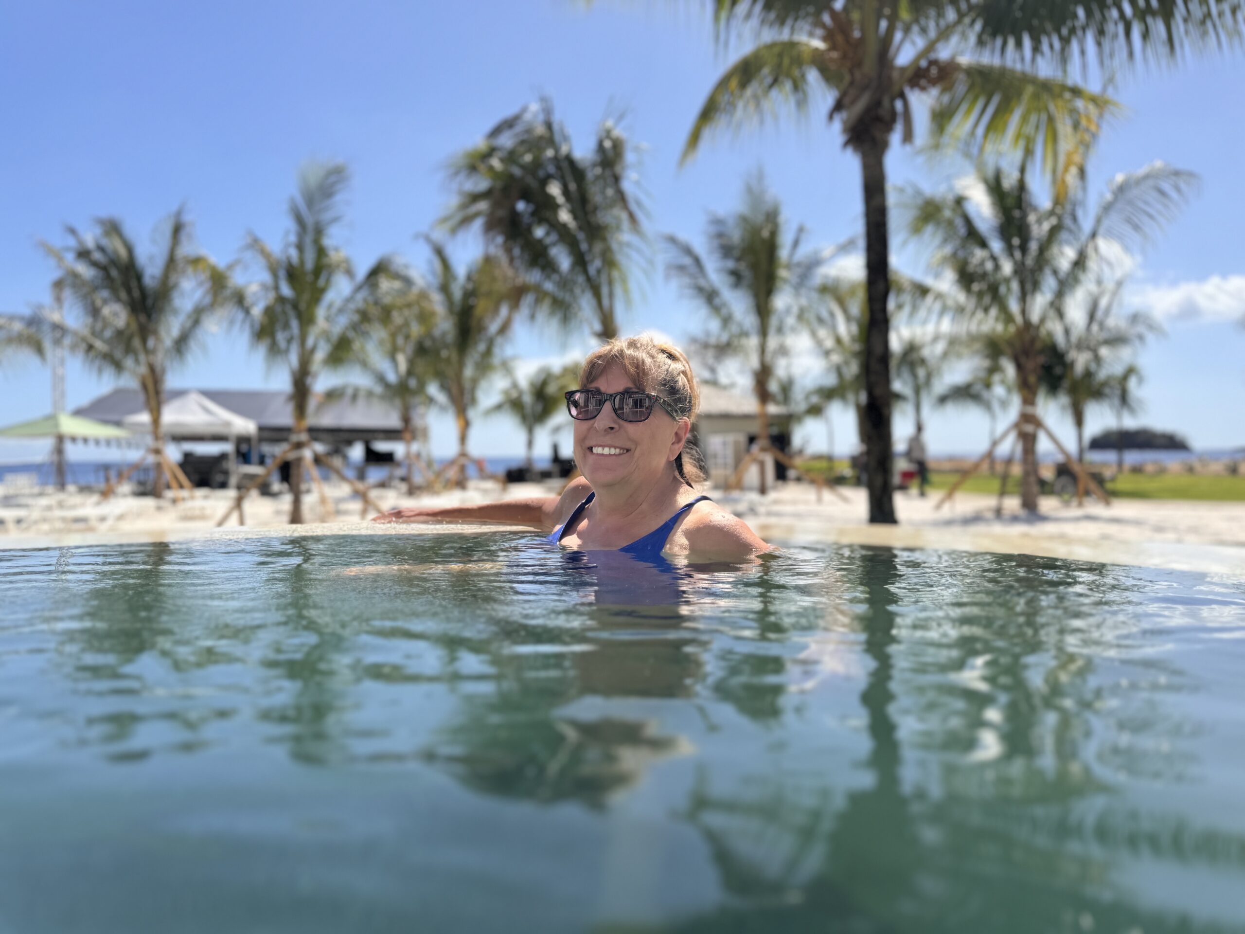 Carol relaxing in the private pool at the Beachfront One-Bedroom Butler Villa Suite with Private Pool (BVJP) at Sandals Saint Vincent, with palm trees and the beach behind