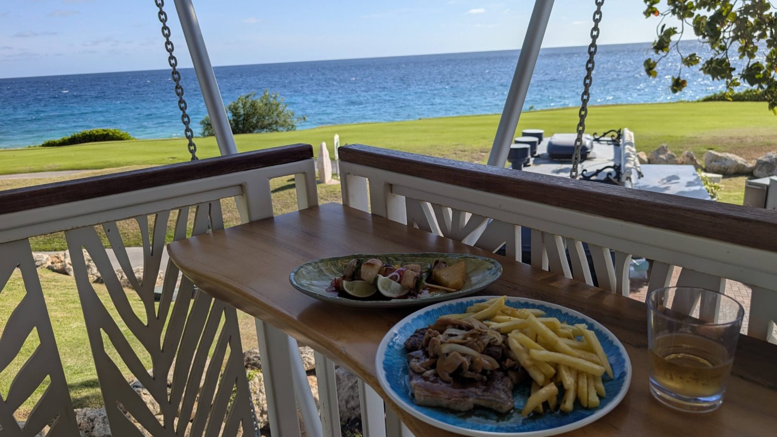 Outdoor dining deck at Sandals Royal Curaçao with steak and seafood skewer overlooking the golf course and ocean