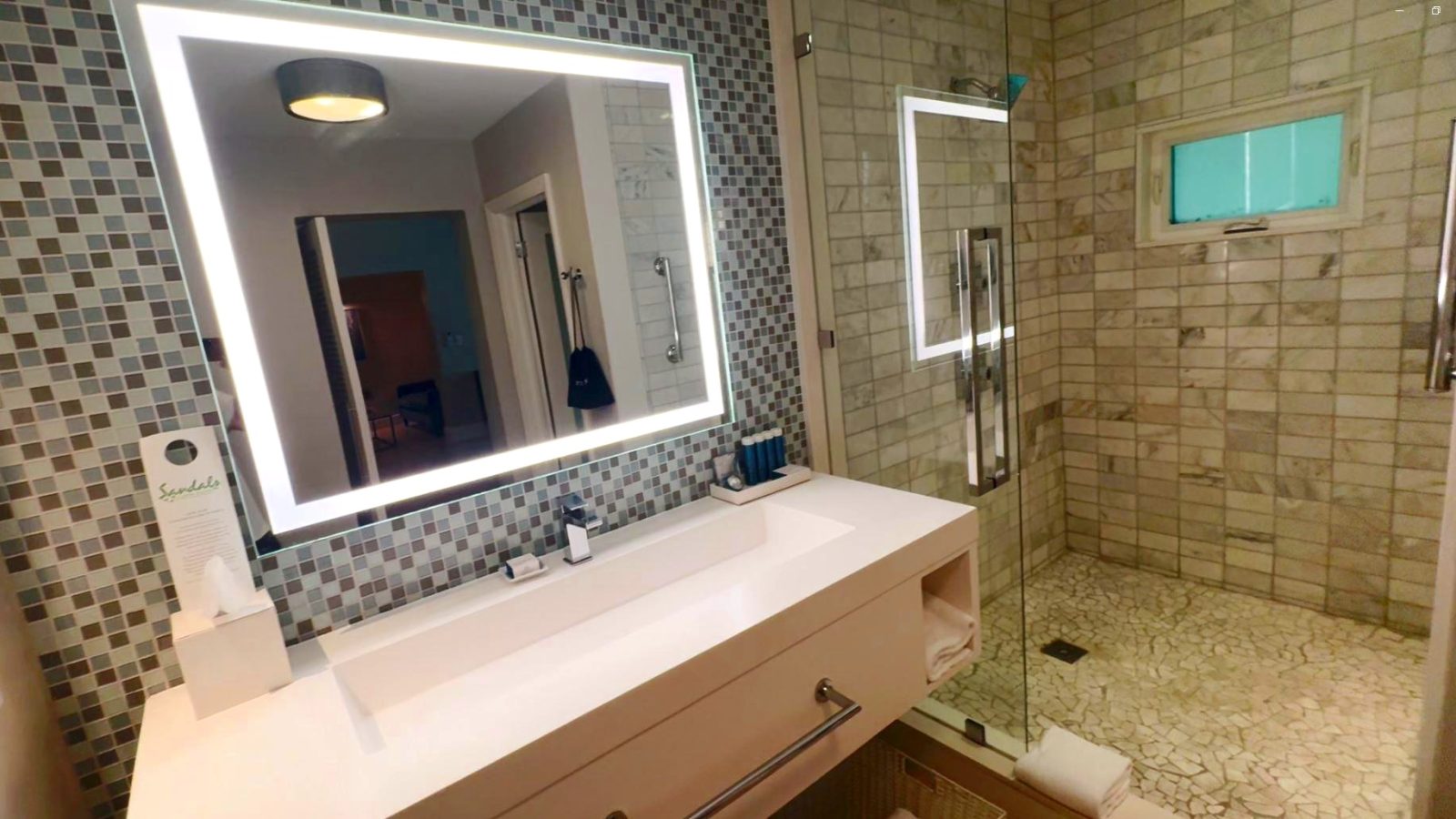 Bathroom in the Island Village One Bedroom Butler Villa Suite (V1PP) at Sandals Royal Bahamian, with a long double sink, backlit mirror, and a walk-in shower