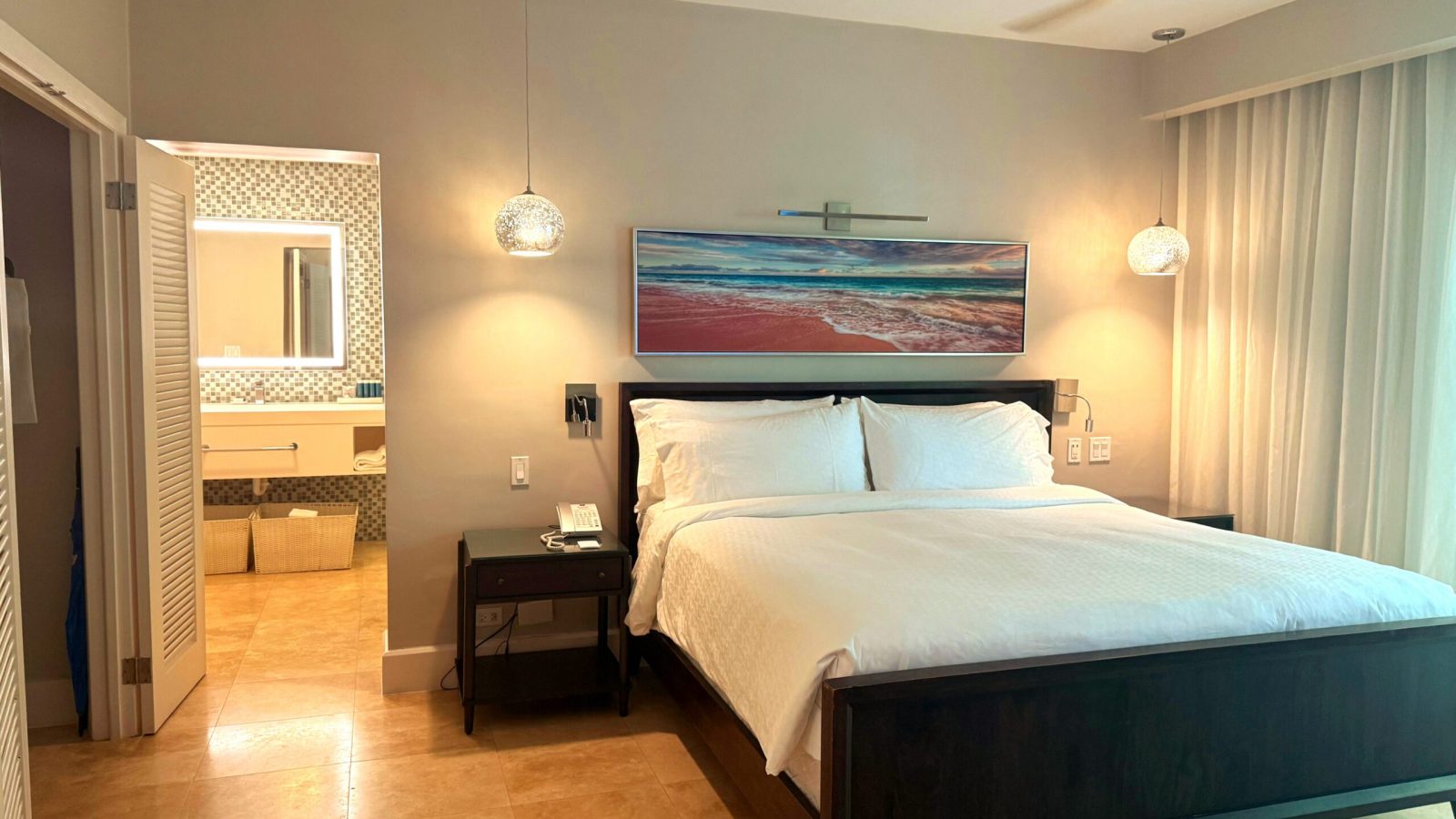 King bedroom in the Island Village One Bedroom Butler Villa Suite (V1PP) at Sandals Royal Bahamian, with an ensuite spa bathroom and ocean artwork above the bed