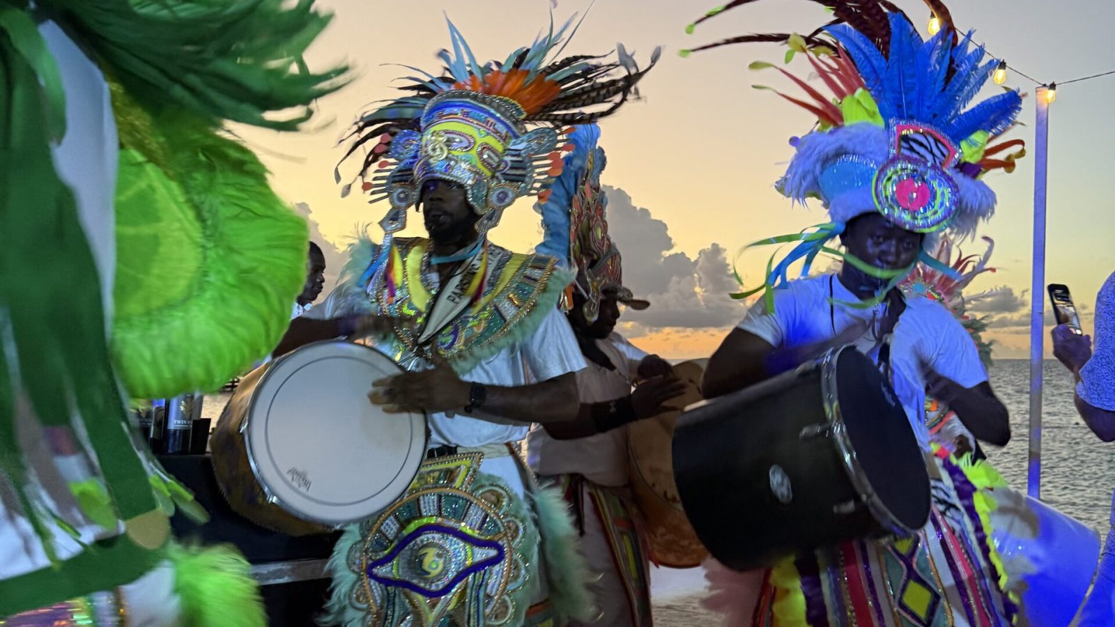 Junkanoo performers in feathered costumes drumming on the beach at sunset at Sandals Royal Bahamian